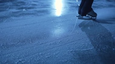 Arenada buz gibi buz üstünde kayan buz pateninin kadın bacakları. Profesyonel bir sporcu kadın karanlıkta mavi ışıkla antrenman yapar. Kadın buzda kayıyor ve duruyor. Kapatın. Yavaş çekim.