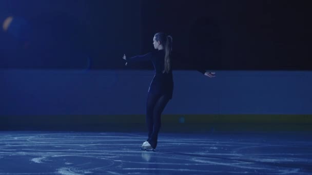 Профессиональный фигурист катается на горках и вращается на ледяной арене в лучах синего света. Молодая женщина репетирует репертуар ледового шоу. Художественный спорт, изящество, точность и совершенство. Медленное движение. — стоковое видео