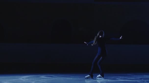 Artiste de patinage artistique professionnel glisse et tourne sur l'arène de glace dans les rayons de lumière bleue. Jeune femme pratiquant le répertoire d'un spectacle de glace. Sport artistique, grâce, précision et perfection. Mouvement lent. — Video
