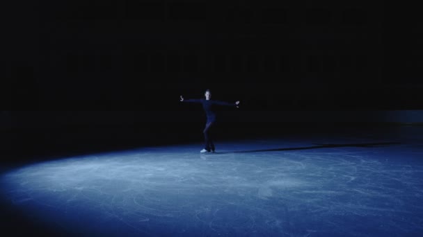 Mulher aparece na arena de gelo em luz azul de holofotes e desliza sobre o gelo, praticando coreografia única. A patinadora feminina está se preparando para habilidades de desempenho e rotação de treinamento. Movimento lento. — Vídeo de Stock