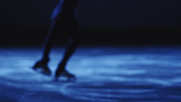 Suddig bild av konståkning dam är skridskor på ishall, utbildning ensam på natten i strålar av blått ljus. Ung kvinna förbereder sig för tävling, utbildning rotation färdigheter. Långsam rörelse, närbild. — Stockvideo