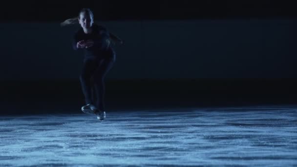 Junge Eiskunstläuferin dreht sich im Dunkeln vor blauem Licht auf der Eisarena. Anmutige Athletin, die Spins für eine Eisshow übt. Eine einzige Choreographie. Zeitlupe. — Stockvideo