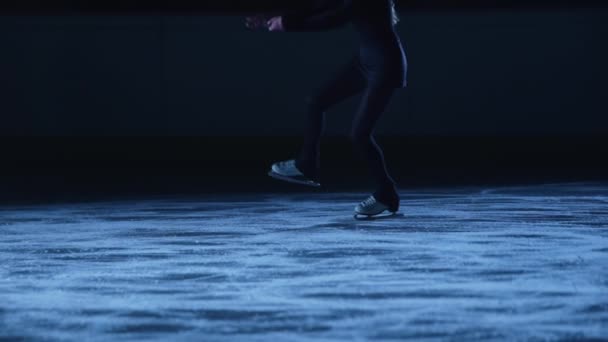 La señora patinadora patinadora está patinando en pista de hielo, entrenando por la noche en los rayos de luz azul. Mujer joven que se prepara para la competencia, el entrenamiento de salto y diapositivas habilidades. Movimiento lento, piernas en patines de cerca. — Vídeos de Stock