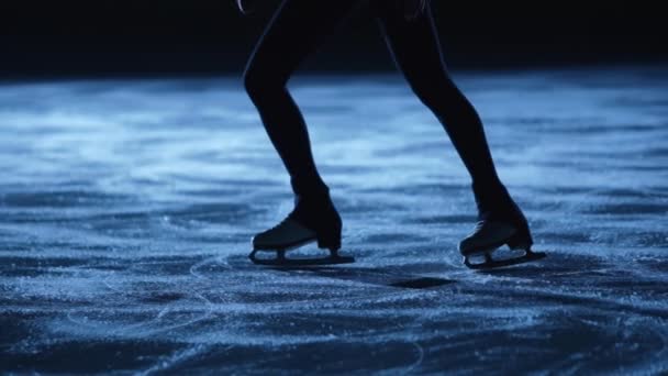 La señora patinadora patinadora está patinando en pista de hielo, entrenando por la noche en los rayos de luz azul. Mujer joven que se prepara para la competencia, la formación de diapositivas habilidades. Movimiento lento, piernas en patines de cerca. — Vídeo de stock