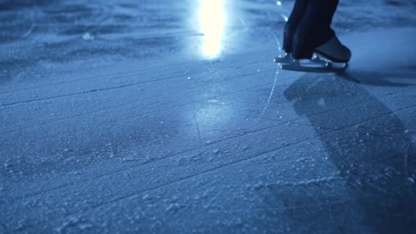 Dettaglio colpo di gambe femminili in pattinaggio artistico pattini scorrevoli su ghiaccio freddo in arena. Una sportiva professionista si allena al buio con la luce blu. La donna scivola sul ghiaccio e si ferma. Chiudete. Rallentatore. — Video Stock