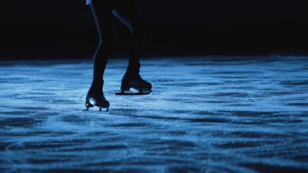 A senhora da patinagem artística está a patinar na pista de patinagem, a treinar à noite nos raios de luz azul. Jovem preparando-se para a competição, treinamento de salto e habilidades de slides. Movimento lento, pernas em patins de perto. — Vídeo de Stock