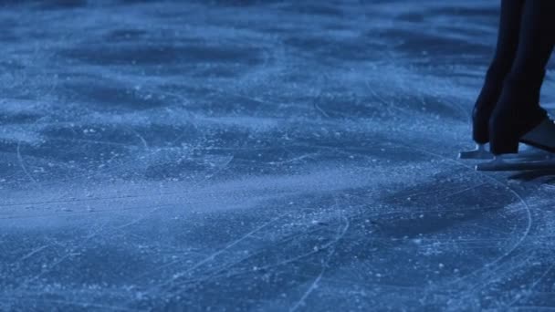 Детальний знімок жіночих ніг у фігурних ковзанах ковзає на холодному льоду на арені. Професійна спортсменка тренується в темряві з синім світлом. Жінка ковзає на льоду і зупиняється. Близько. Повільний рух . — стокове відео