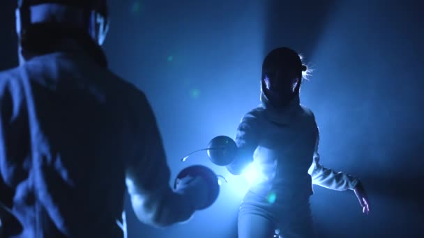从后面看两个运动员击剑比赛.戴着护目镜的妇女互相攻击，用epee一击。黑暗工作室背光蓝光和烟雾。慢动作靠近点. — 图库视频影像