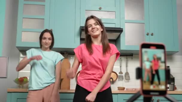 Két fiatal lány táncol és videókat készít blogjaiknak vagy közösségi oldalaiknak. Bloggerek rögzítik vlog trend tartalmát a konyhában. Online tartalom, történetek. Lassú mozgás kész, 4K 59.97fps-en.. — Stock videók
