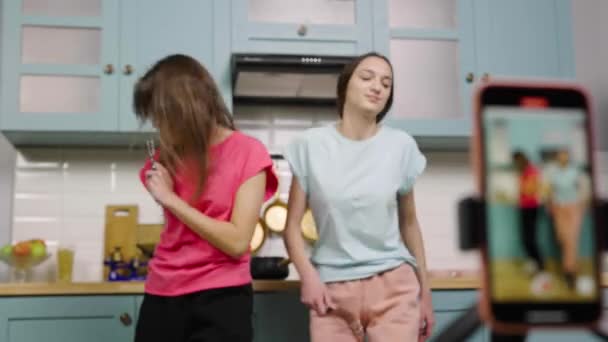 Two young girls dancing, sing and filming videos for their blogs or social networks. Bloggers are recording vlog with trend content in kitchen. Slow motion ready, 4K at 59.97fps. — Stock Video