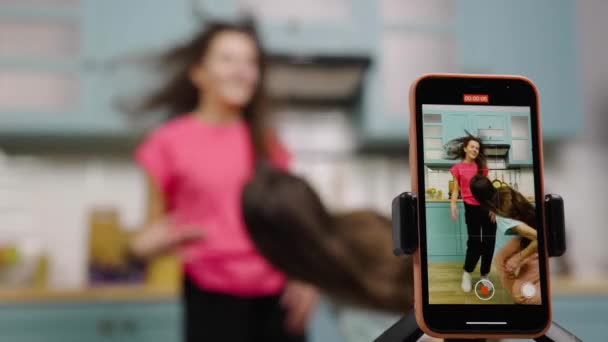 Dua gadis muda menari, bernyanyi, bersenang-senang dan merekam video untuk blog mereka atau jejaring sosial. Narablog merekam vlog dengan tren konten di dapur. Gerakan lambat siap, 4K di 59.97fps. — Stok Video