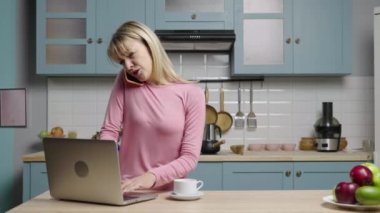 Genç kadın dizüstü bilgisayarda çalışıyor, telefonla konuşuyor ve çok üzgün. Aile blogcuları sosyal medya ve video blogu için mutfakta hikayeler kaydediyor. Ağır çekim hazır, 4K 59.97 fps 'de..