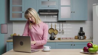 Genç kadın dizüstü bilgisayarda çalışıyor, telefonla konuşuyor ve çok üzgün. Aile blogcuları sosyal medya ve video blogu için mutfakta hikayeler kaydediyor. Ağır çekim hazır, 4K 59.97 fps 'de..