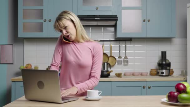 Mujer joven está trabajando en el ordenador portátil, hablando por teléfono y está muy molesto. Los bloggers familiares filman historias en la cocina para los medios sociales y el video blog de la vida. Cámara lenta lista, 4K a 59.97 fps. — Vídeo de stock