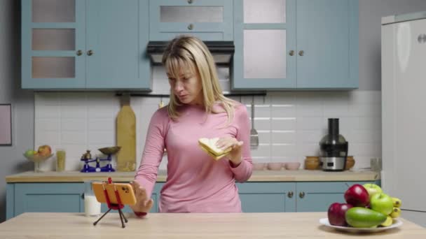 Mujer joven viendo videos divertidos en las redes sociales usando el teléfono, comiendo sándwich y riendo. La blogger está filmando historias para redes sociales y video blog de la vida. Cámara lenta lista, 4K a 59.97 fps. — Vídeo de stock