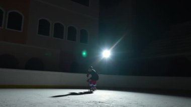 Karanlık bir buz arenasında spot ışıklarıyla hokey oynayan bir sporcu. Üniformalı bir kask ve elinde sopayla ileri doğru kayarak bir gol atıyor. Hokey diski kaleye çarptı. Yavaş çekim.