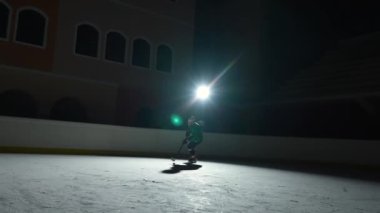 Profesyonel forvet oyuncusu usta bir şekilde top sürüyor, puck 'a sopa puanı golüyle vuruyor. Hokey diski ağa çarptı. Karanlık buz arenasında spot ışıklarıyla hokey oynayan bir atlet. Yavaş çekim.