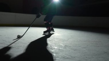 Düşük açı hokey forvet oyuncusu usta bir şekilde top sürüyor ve puck 'a sopa puanı golüyle vuruyor. Hokey diski ağa çarptı. Karanlık buz arenasında spot ışıklarıyla hokey oynayan bir atlet. Yavaş çekim.