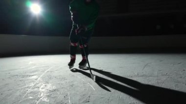 Düşük açı hokey forvet oyuncusu usta bir şekilde top sürüyor ve puck 'a sopa puanı golüyle vuruyor. Hokey diski ağa çarptı. Karanlık buz arenasında spot ışıklarıyla hokey oynayan bir atlet. Yavaş çekim.