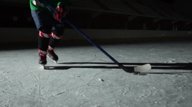 Düşük açı hokey forvet oyuncusu usta bir şekilde top sürüyor ve puck 'a sopa puanı golüyle vuruyor. Hokey diski ağa çarptı. Karanlık buz arenasında spot ışıklarıyla hokey oynayan bir atlet. Yavaş çekim.