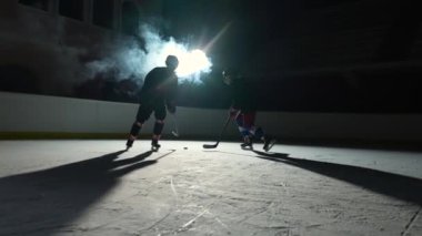 Üniformalı iki hokey oyuncusu puck 'a sopayla vuruyor ve golü atıyor. Hokey diski ağa çarptı. Sporcular karanlık buz arenasında spot ışıklarıyla hokey oynarlar. Yavaş çekim.