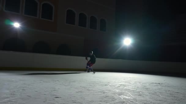 Profi-Stürmer dribbelt meisterhaft und trifft den Puck mit dem Stock ins Tor. Eishockey-Puck landet im Netz. Ein Sportler spielt Hockey auf einer dunklen Eisarena mit Scheinwerfern. Zeitlupe. — Stockvideo