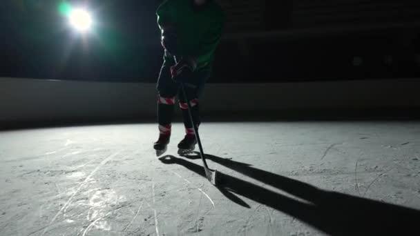 Low angle hockey forward player masterfully dribbles, hitting puck with stick scores goal. Hockey puck hits the net. An athlete man plays hockey on dark ice arena with spotlights. Slow motion. — Stock Video