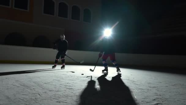 Dva muži hokejista v uniformách mistrovsky dribbles, bít puk s holí a dopředu skóre gól. Hokejový puk udeřil do sítě. Sportovci hrají hokej na tmavé ledové aréně s reflektory. Zpomalený pohyb.