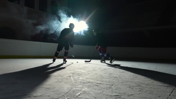 Zwei Hockeyspieler in Uniformen dribbeln meisterhaft, treffen den Puck mit dem Stock und erzielen das Tor. Eishockey-Puck landet im Netz. Die Athleten spielen Hockey auf einer dunklen Eisarena mit Scheinwerfern. Zeitlupe. — Stockvideo