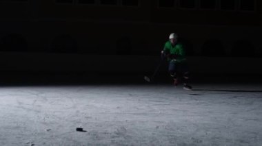 Yeşil üniformalı ve elinde sopa olan bir miğfer buzda kayıyor ve diske vuruyor. Karanlık bir arenanın buzunda arka ışığı olan bir atlet paten kayar. Yavaş çekim.