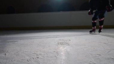 Bir hokey oyuncusu karanlık bir buz arenasında ışıklarla kayıyor, hokey sopasıyla buza çarpıyor ve kameraya buz tozu atıyor. Sinema yavaş çekim. Buz arenasını kapatın..