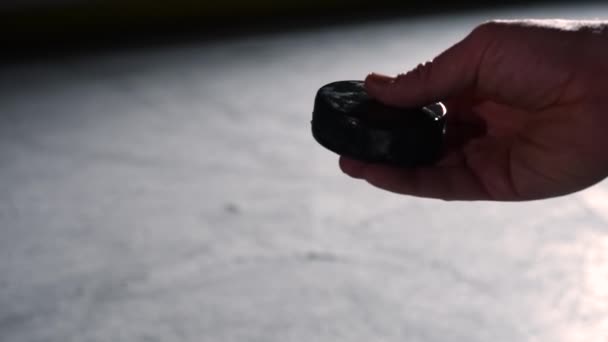 Une main d'homme lance la rondelle de hockey noire sur la glace de l'aréna pour commencer la compétition. Les bâtons de hockey frappent la rondelle. Tournoi de hockey sportif sur patinoire avec rétroéclairage. Au ralenti. Gros plan. — Video