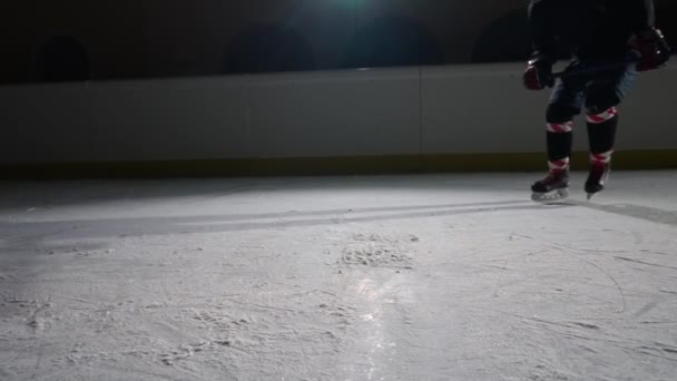 Хокеїст ковзає по темній льодовій арені з вогнями, влучає в лід з хокейною палицею і кидає в камеру крижаний порох. Кінематографічний повільний рух. Близько льодовикової арени . — стокове відео