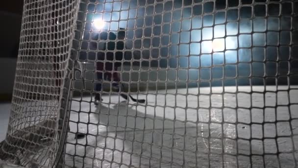 Ein Blick hinter das Netz des Eishockey-Stürmers, der den Puck mit dem Stock trifft und ein Tor erzielt. Nahaufnahme eines Eishockeypucks in Zeitlupe, der ins Netz fliegt. Dunkle Eishockey-Arena mit Scheinwerfern und Rauch. — Stockvideo