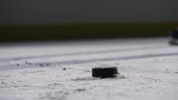 Сосредоточьтесь на черной шайбе хоккей лежал на льду катка. Хоккеист скользит по арене и попадает шайбу с хоккейной клюшкой, разрезая лед в порошок. Кинематографическая задержка. Закрыть — стоковое видео