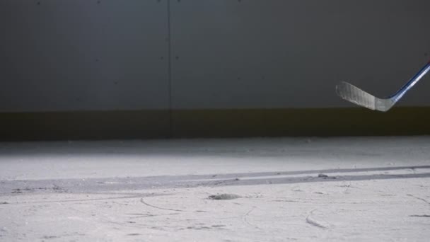 Ένας παίκτης χόκεϊ γλιστρά σε μια σκοτεινή αρένα πάγου με φώτα, χτυπά τον πάγο με ένα ραβδί χόκεϊ και ρίχνει σκόνη πάγου στην κάμερα. Κινηματογραφική αργή κίνηση. Κοντινό πλάνο της αρένας πάγου. — Αρχείο Βίντεο