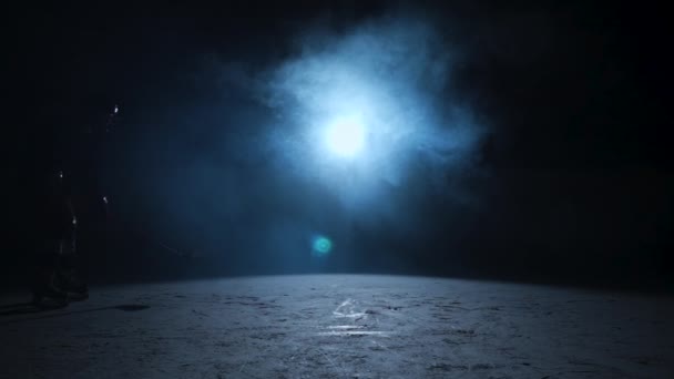 Dark silhouettes of two male hockey players in a uniform, helmet and with stick in his hands, skating on ice. An athletes posing on the ice of dark arena with blue backlight and smoke. Slow motion. — Stock Video