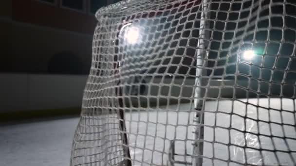 Hokejový puk zasáhne síť, vstřelil gól. Detailní záběr pomalého hokejového puku letícího do sítě. Film za brankami široký záběr. Tmavá hokejová aréna s reflektory. — Stock video