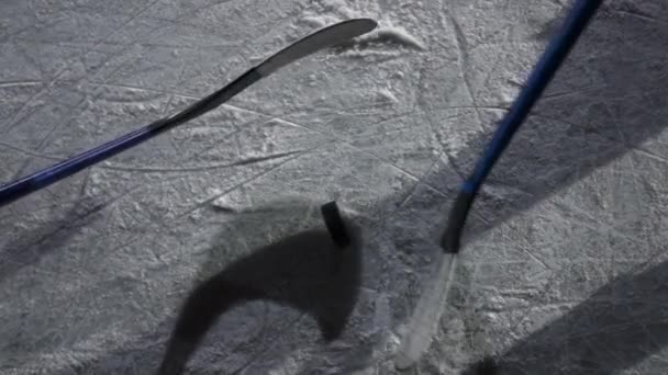 Vista superior del disco de hockey negro que cae sobre hielo de la pista. Un jugador de hockey se desliza por la arena y golpea el disco con un palo de hockey. Grabación cinematográfica en cámara lenta con reflejos y sombras. De cerca.. — Vídeo de stock