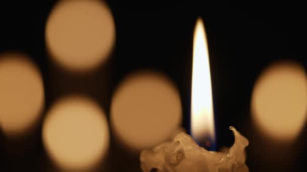 Vela ardiente de cera parpadea en la oscuridad sobre un fondo negro con efecto bokeh vela borrosa. Antecedentes o ilustración de recuerdo, luto o celebración. Encender velas en la iglesia de cerca. — Vídeos de Stock