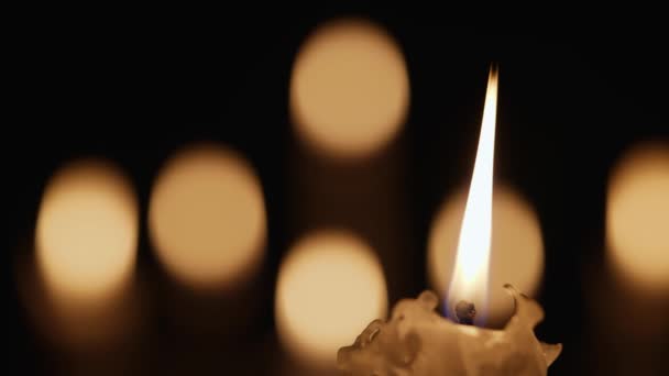 La cire qui brûle la bougie scintille dans l'obscurité sur un fond noir avec un effet bokeh flou aux bougies. Contexte ou illustration du souvenir, du deuil ou de la célébration. Bougies flamboyantes dans l'église fermer. — Video