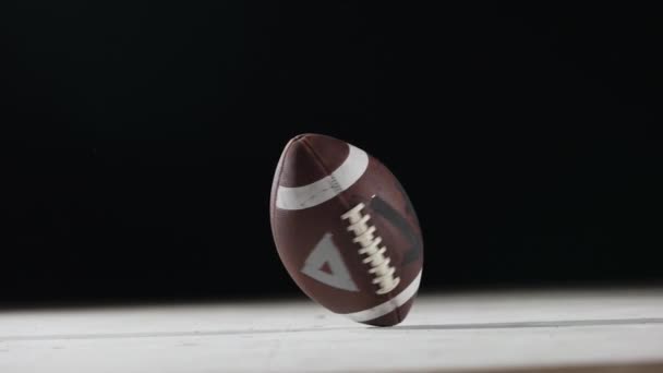 Americký fotbal rotuje na černém pozadí zblízka. Oválný americký fotbalový míček se otáčí ve zpomaleném filmu na podsvíceném stadiónu. Extrémní sportovní koncept. Mužská agresivní hra. — Stock video