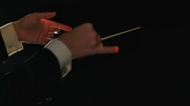 Müzisyenleri yöneten bir orkestra şefinin ellerini hareket ettirerek siyah arka planda ışıklar eşliğinde sopalarını hareket ettiriyorlar. Görünür jestlerle klasik müzik performanslarını yönetmek. Kapat..