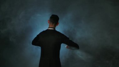 Senfoni orkestra şefi. Maestro siyah duman arka planı ve arka planda baton hareketleriyle müzisyenleri yönetiyor. Görünür jestlerle müzik performanslarını yönetmek. Kapat..