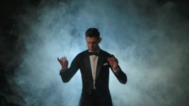 Müzisyenleri senkronize etmek için sopa kullanan bir orkestra lideri. Maestro siyah arka planda dumanlı ve arka planda sopa hareketleriyle müzisyenleri yönetiyor. Kapat..