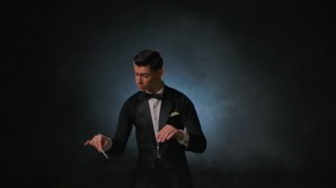 Müzisyenleri senkronize etmek için sopa kullanan bir orkestra lideri. Maestro siyah arka planda dumanlı ve arka planda sopa hareketleriyle müzisyenleri yönetiyor. Kapat..