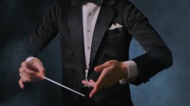 Bir orkestra şefinin yönetiminde klasik müzik konseri. Adam tiyatroda müzisyenleri senkronize etmek ve yönetmek için sopasını sallıyor. Duman ve arka planda siyah arka plan. Kapat..