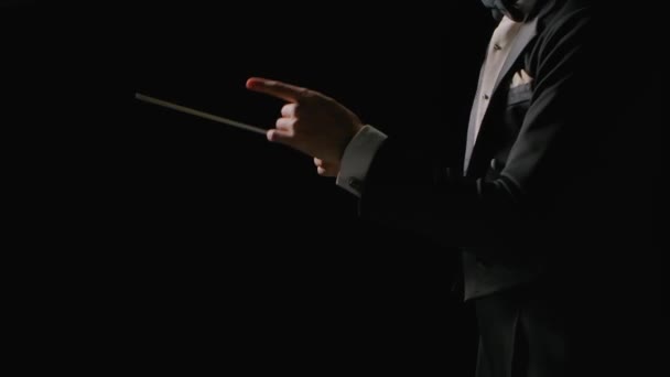 Konduktor orkestra simfoni mengenakan setelan mengarahkan musisi dengan gerakan tongkat, terisolasi di latar belakang hitam. Melakukan, mengarahkan pertunjukan musik dengan gerakan yang terlihat. Tutup.. — Stok Video