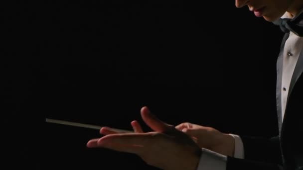 Симфонічний диригент оркестру в костюмі режисує музикантів з рухом палички, ізольовані на чорному тлі. диригування, режисура музичного виступу з видимими жестами. крупним планом . — стокове відео