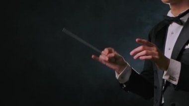Bir orkestra şefinin yönetiminde klasik müzik konseri. Adam tiyatroda müzisyenleri senkronize etmek ve yönetmek için sopasını sallıyor. Duman ve arka planda siyah arka plan. Kapat..